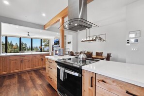 Une cuisine moderne avec des meubles en bois, un poêle noir et une grande fenêtre donnant sur une forêt.