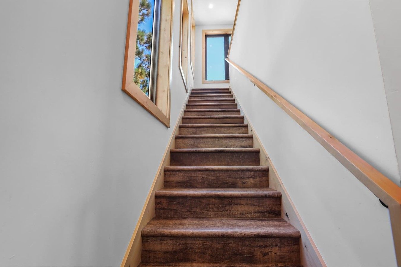 A wooden staircase with a handrail, leading to a room with a window.