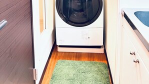 Ett kompakt tvättrum med en tvättmaskin med frontmatning, en liten grön matta och ett trägolv.
