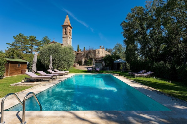 Relax by the serene pool surrounded by lush greenery and a historic tower.
