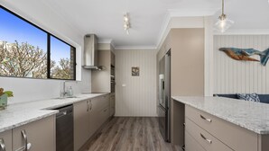 Una cocina moderna con suelo de madera, electrodomésticos de acero inoxidable y un amplio ventanal con vistas a árboles.