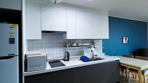 A modern kitchen with white cabinets, a black countertop, a sink, and a refrigerator. - Kkomasi pension (Boseong)