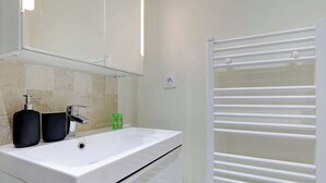 Un baño con un lavamanos blanco, dos dispensadores de jabón negros, una botella verde y un perchero blanco.