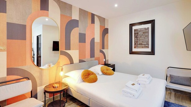 Una habitación de hotel moderna con una cama grande, un espejo redondo, una mesita con una lámpara y un mapa enmarcado en la pared.