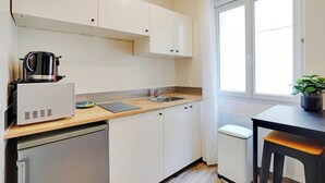 Una cocina compacta con armarios blancos, un lavamanos, una cafetera y un refrigerador pequeño.