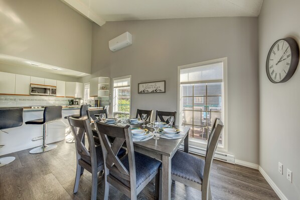 Una cocina moderna con armarios blancos, un microondas y un comedor con mesa y sillas de madera.