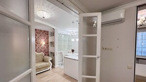 Un couloir avec un canapé beige, une coiffeuse blanche avec un miroir et un lustre.