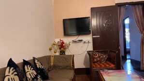 A living room with a sofa, a television mounted on the wall, a dining table with chairs, and a door leading to another room. - Hotel B&B Heights (Guwahati)