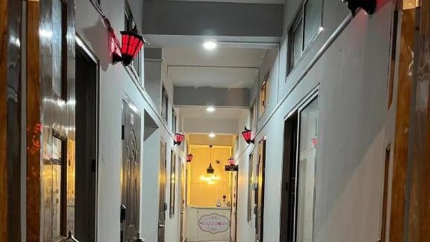 A narrow hallway with wooden doors on both sides, potted plants, and red wall-mounted lights. - Hotel B&B Heights (Guwahati)