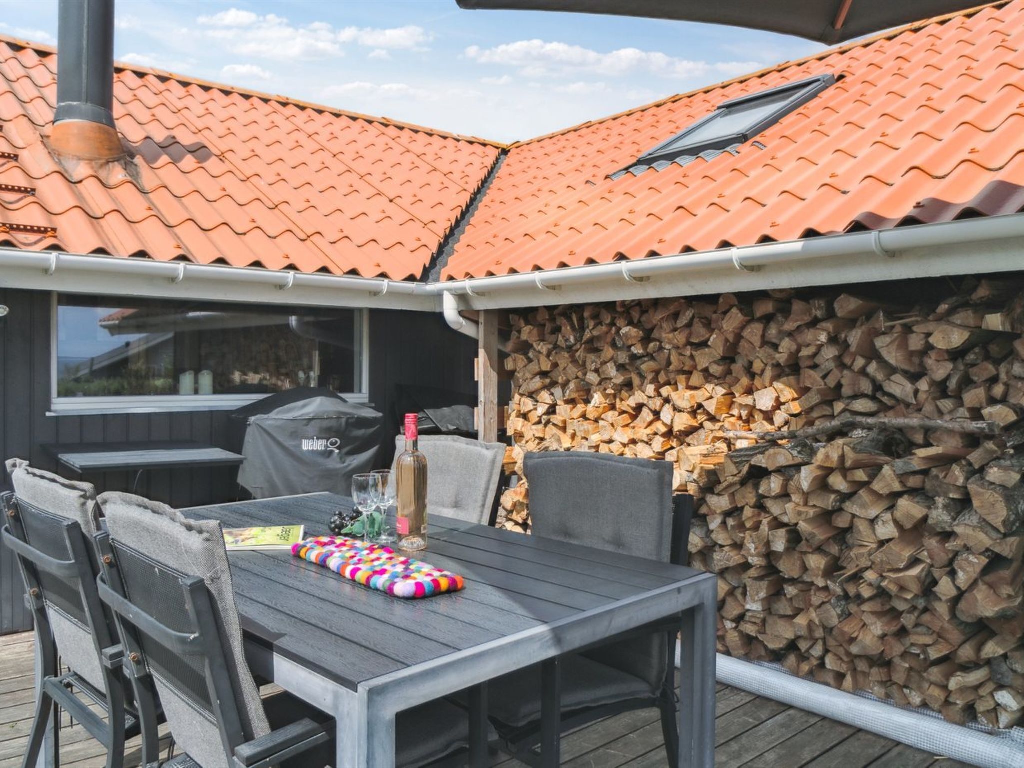 Eine Terrasse im Freien mit Tisch, Stühlen, einem Grill und einem Holzstapel.