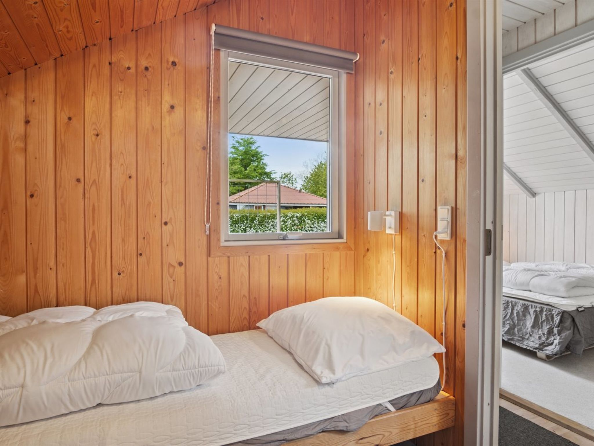A wooden-paneled room with a bed, a window, and a door leading to another room.