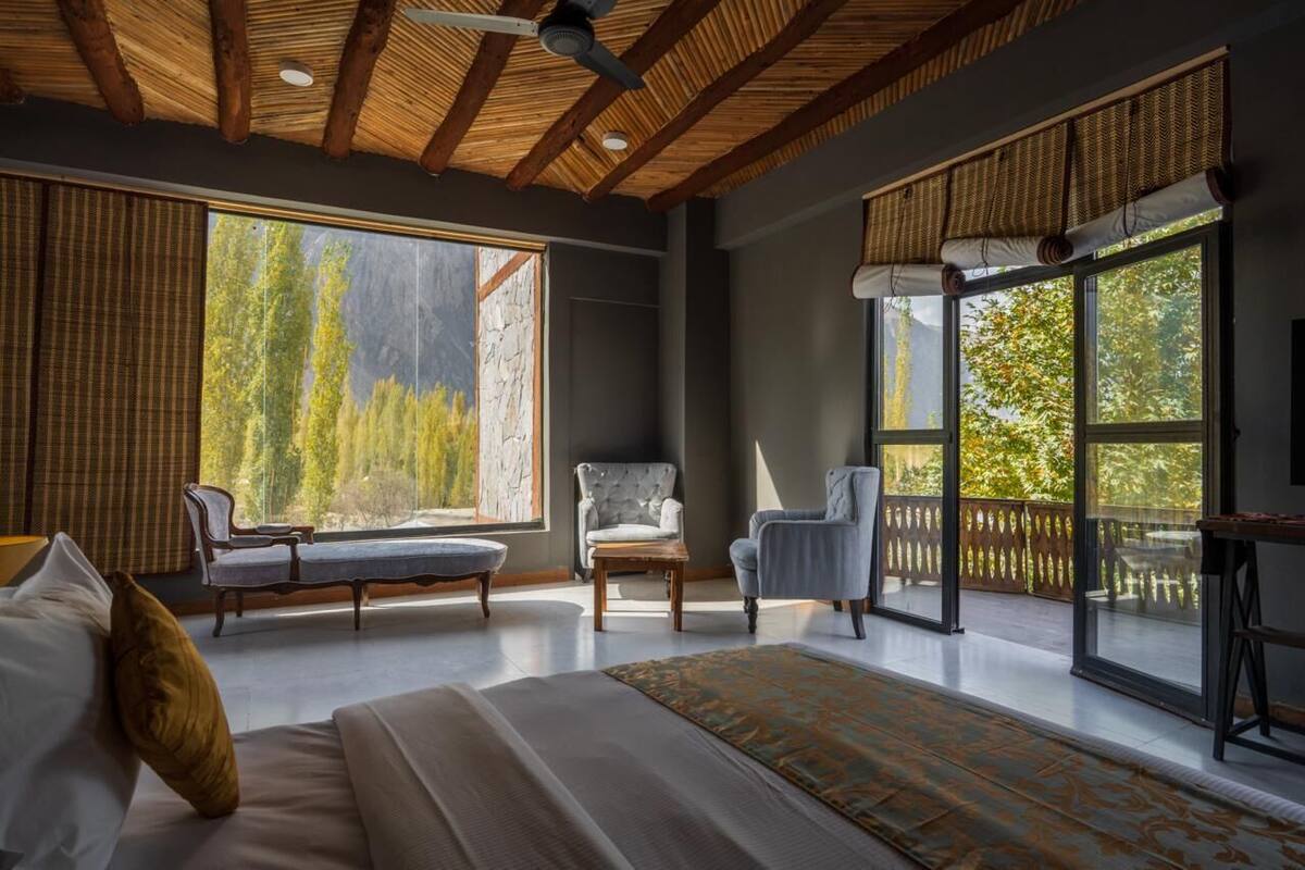A spacious bedroom with a large bed, two chairs, and a view of trees through large windows.