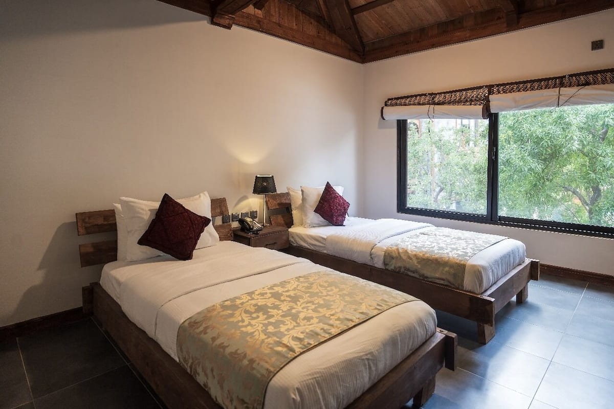 A bedroom with two beds, wooden headboards, and a large window with a view of trees.