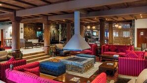 A spacious lobby with a stone fireplace, red and blue upholstered seating, and wooden beams on the ceiling. - PC Legacy Skardu (Skardu)