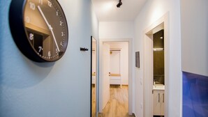 Un pasillo con un reloj en la pared, una puerta que da a una habitación y una vista parcial de un baño.