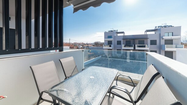 Una terraza en la azotea con una mesa y sillas de vidrio, con vistas a un paisaje urbano.