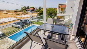 Ein Balkon mit Glastisch, Stühlen und Blick auf einen Pool und geparkte Autos.
