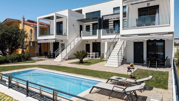 Ein modernes, zweistöckiges Haus mit Pool, Sitzgelegenheiten im Freien und einer Treppe, die zum Obergeschoss führt.