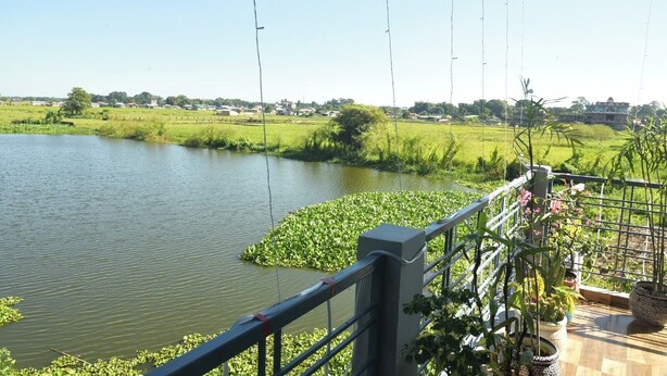 A riverside view with a railing, potted plants, and a clear sky. - Hotel Royal Awas (Biswanath)