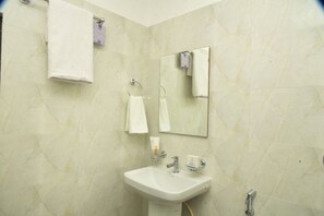 A bathroom with a white sink, two towel rings, a mirror, and a handheld showerhead. - Hotel Royal Awas (Biswanath)