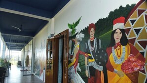 A hallway with a mural depicting cultural figures, a wooden door, and a ceiling fan. - Hotel Royal Awas (Biswanath)