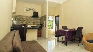 A compact living space with a kitchenette, a dining area with a table and chairs, and a sofa. - Hotel Royal Awas (Biswanath)