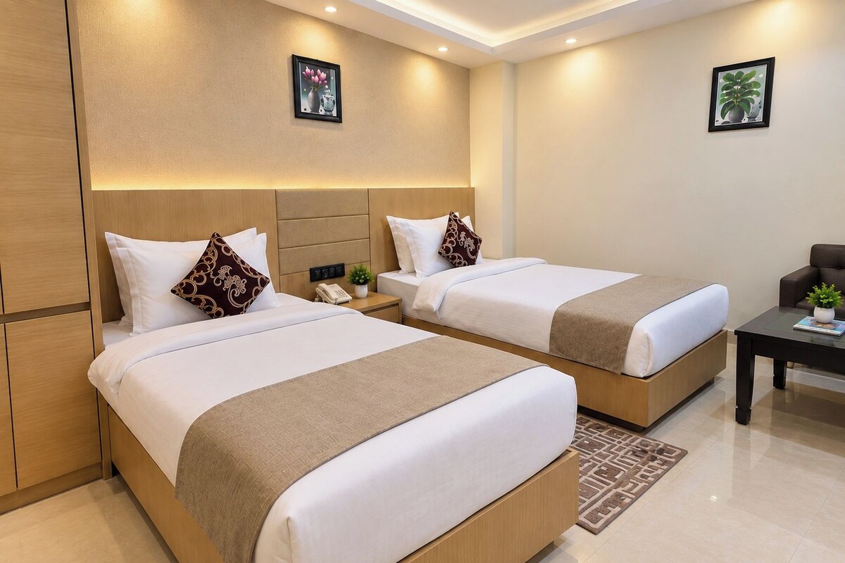A hotel room with two beds, a small table, a chair, and a wall-mounted phone.