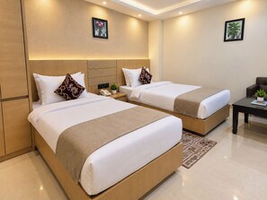 A hotel room with two beds, a small table, a chair, and a wall-mounted phone. - Hotel Royal Awas (Biswanath)
