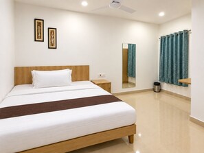 Habitación de hotel con cama, mesita de noche, espejo, ventana con cortinas y ventilador de techo.