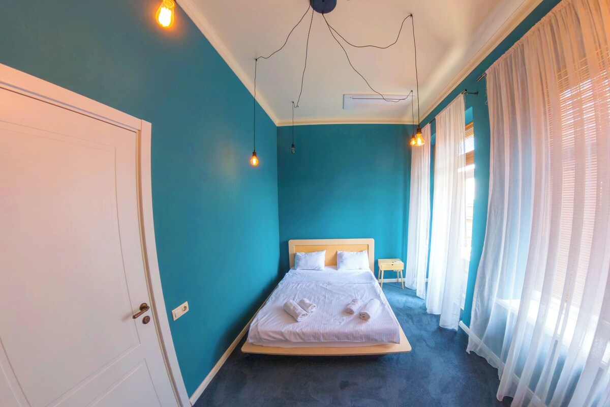 A bedroom with a bed, a nightstand, and a window with curtains.