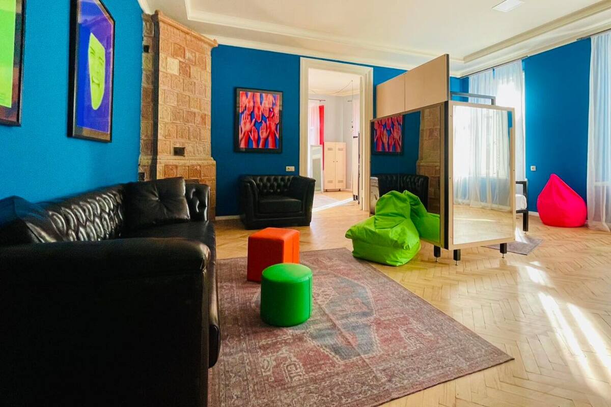 A living room with a black sofa, a green ottoman, a red bean bag, and a mirror.