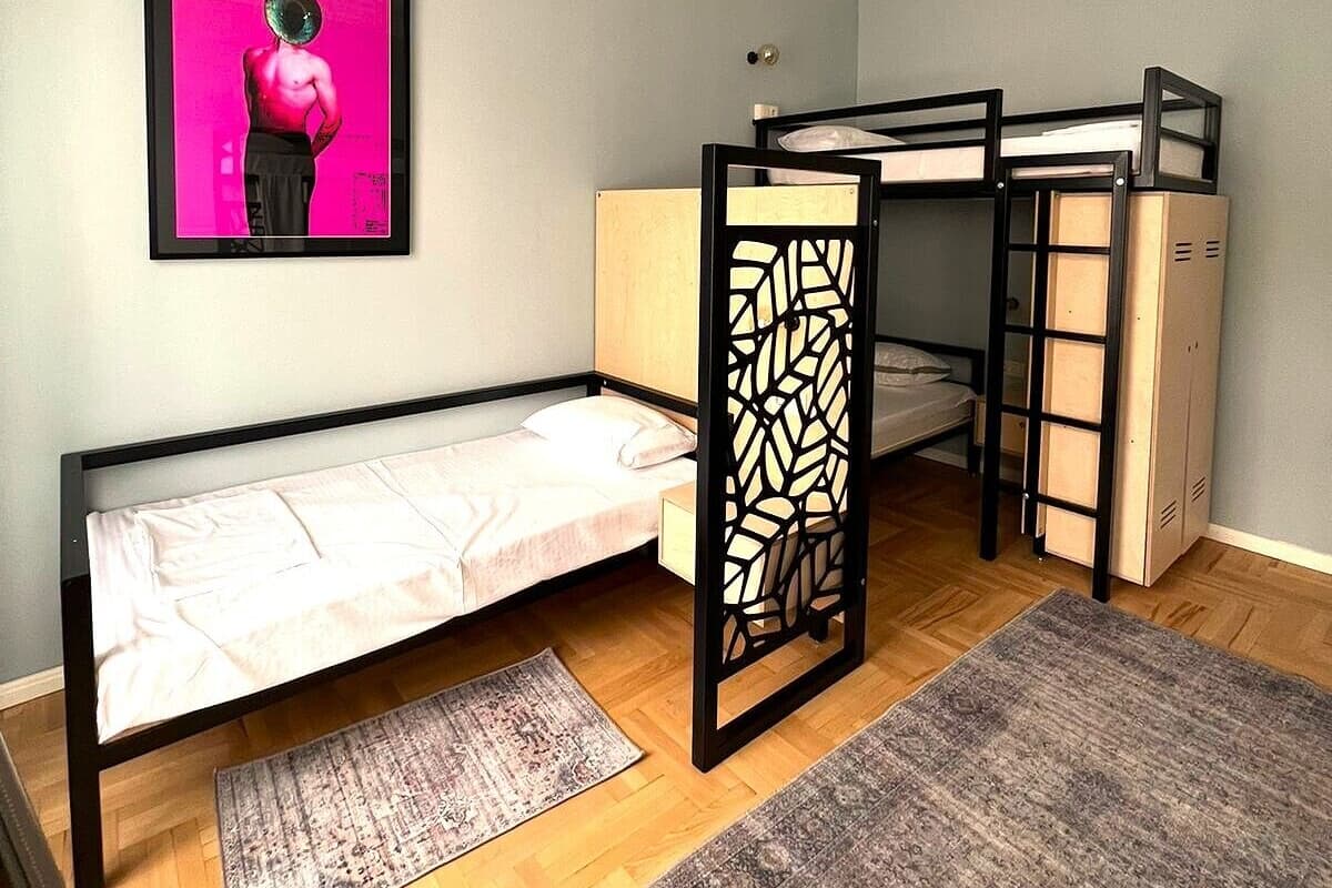 A compact room with a bunk bed, a single bed, a framed artwork on the wall, and a small rug on the floor.