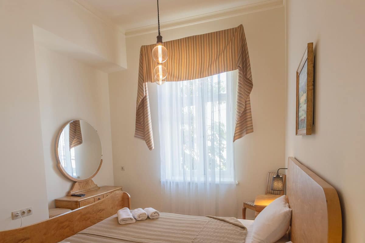 A hotel room with a bed, bedside table, lamp, bedside table lamp, bedside table clock, and a window with curtains.