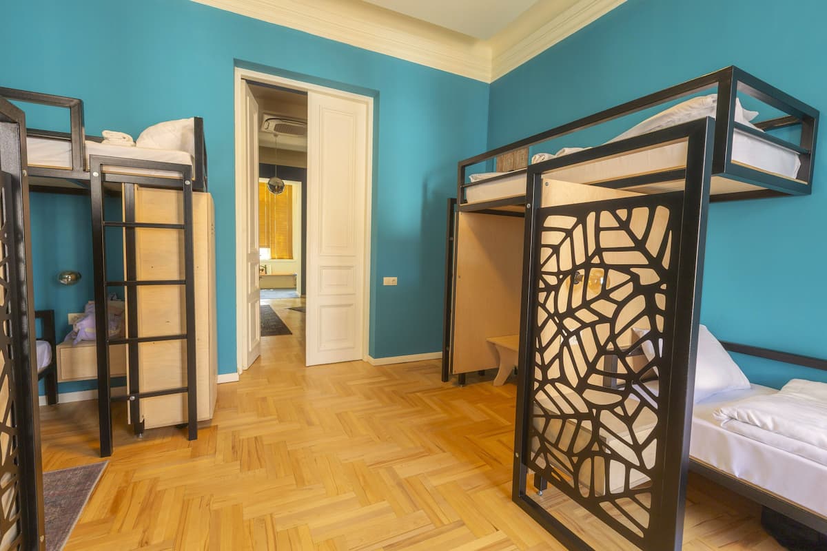 A room with bunk beds, a wooden floor, and a door leading to another room.