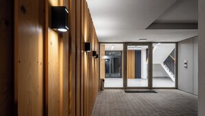 Un couloir moderne avec un lambris en bois, une porte en verre donnant sur un escalier et un luminaire fixé au mur.