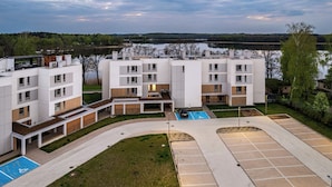 Un immeuble moderne à plusieurs étages, doté d’une cour intérieure, de places de stationnement et offrant une vue sur un lac.