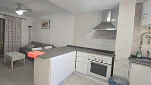 A compact kitchen with a stove, oven, and a small dining area with a table and a sofa. - MARISCAL 3  2I (1  BEDROOM) (Benidorm)