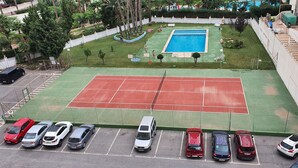 A tennis court with a pool, surrounded by a fence and trees. - MARISCAL 3  2I (1  BEDROOM) (Benidorm)