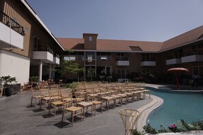 A poolside area with rows of wooden chairs and tables, a swimming pool, and a building with balconies. - Baba Resort (Nandurbar)
