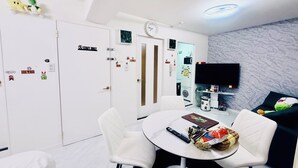 Habitación de hotel moderna con una mesa de comedor redonda, sillas blancas, un televisor de pantalla plana y un sofá.