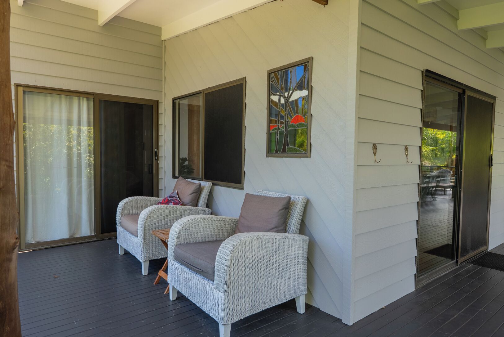 A covered outdoor seating area with wicker furniture and a glass door leading to a patio.