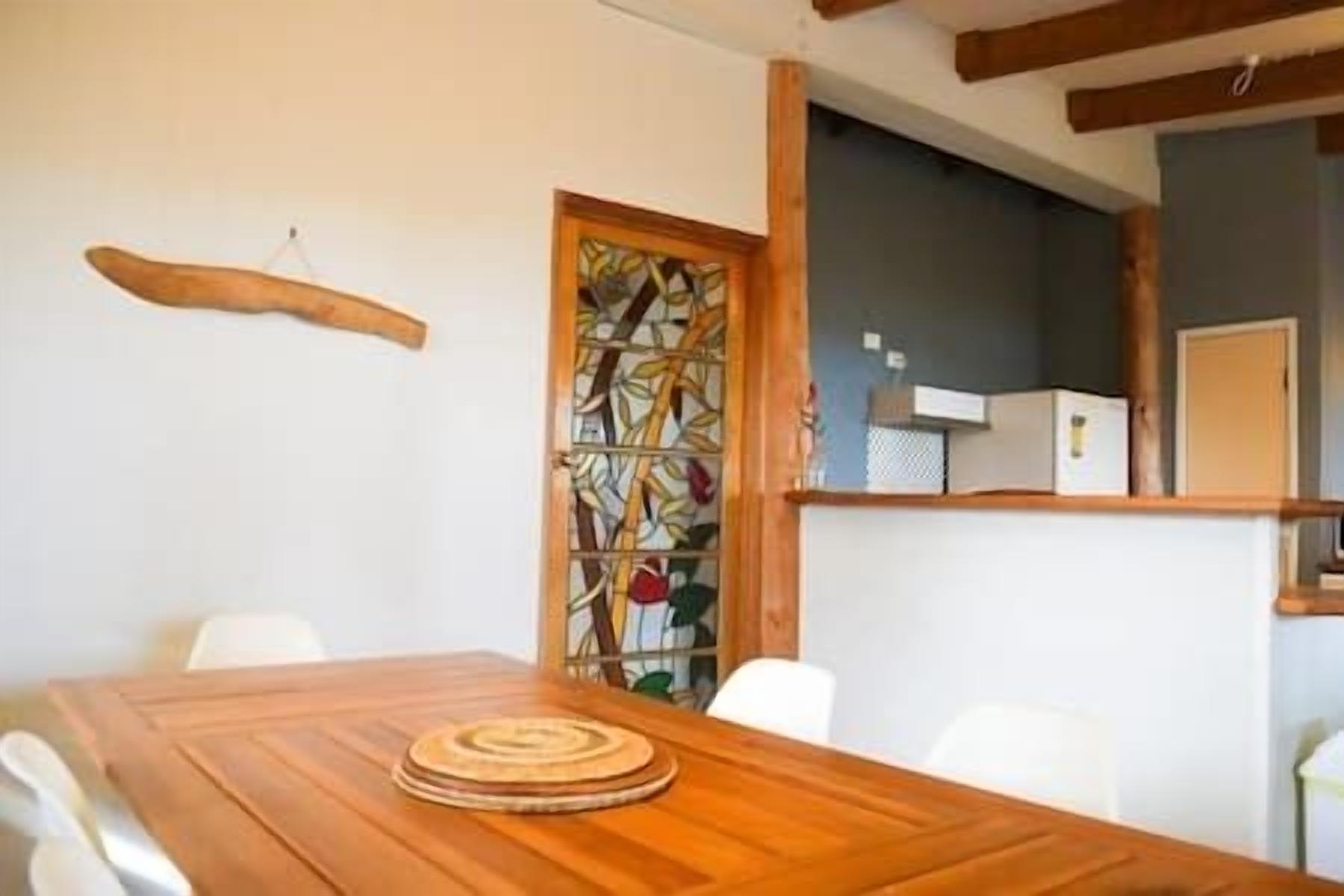 A wooden dining table with a woven placemat, white chairs, and a stained glass door.