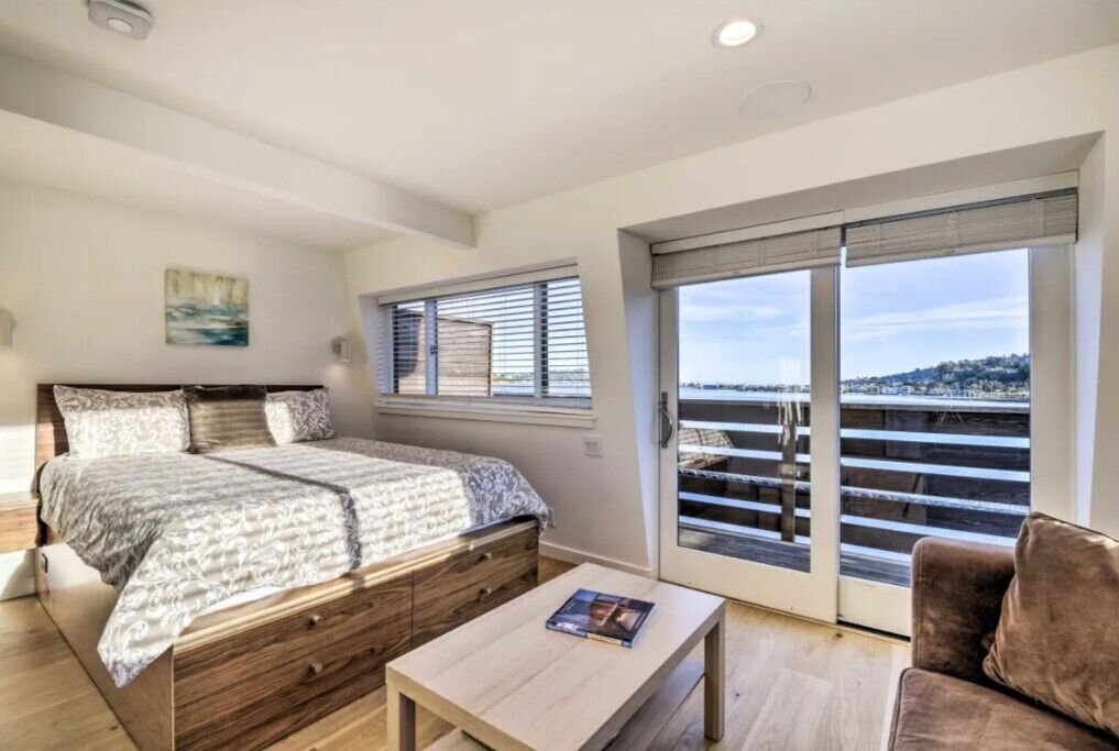 A bedroom with a bed, a wooden dresser, a coffee table, and a balcony with a view.