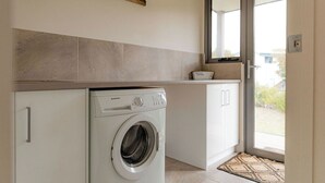 A compact laundry area with a front-loading washing machine, a small sink, and a window above the sink.