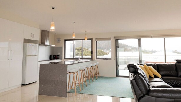 A modern kitchen with a central island, bar stools, and large windows offering a view of the sea.