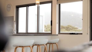 A modern kitchen with a large window, a clock, and two bar stools.