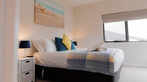 A bedroom with a bed, a nightstand, a window, and a painting on the wall.