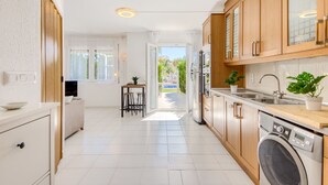 A modern kitchen with wooden cabinets, a built-in washing machine, and a dining area with a table and chairs. - Puerto Rico by Interhome (Empuriabrava)