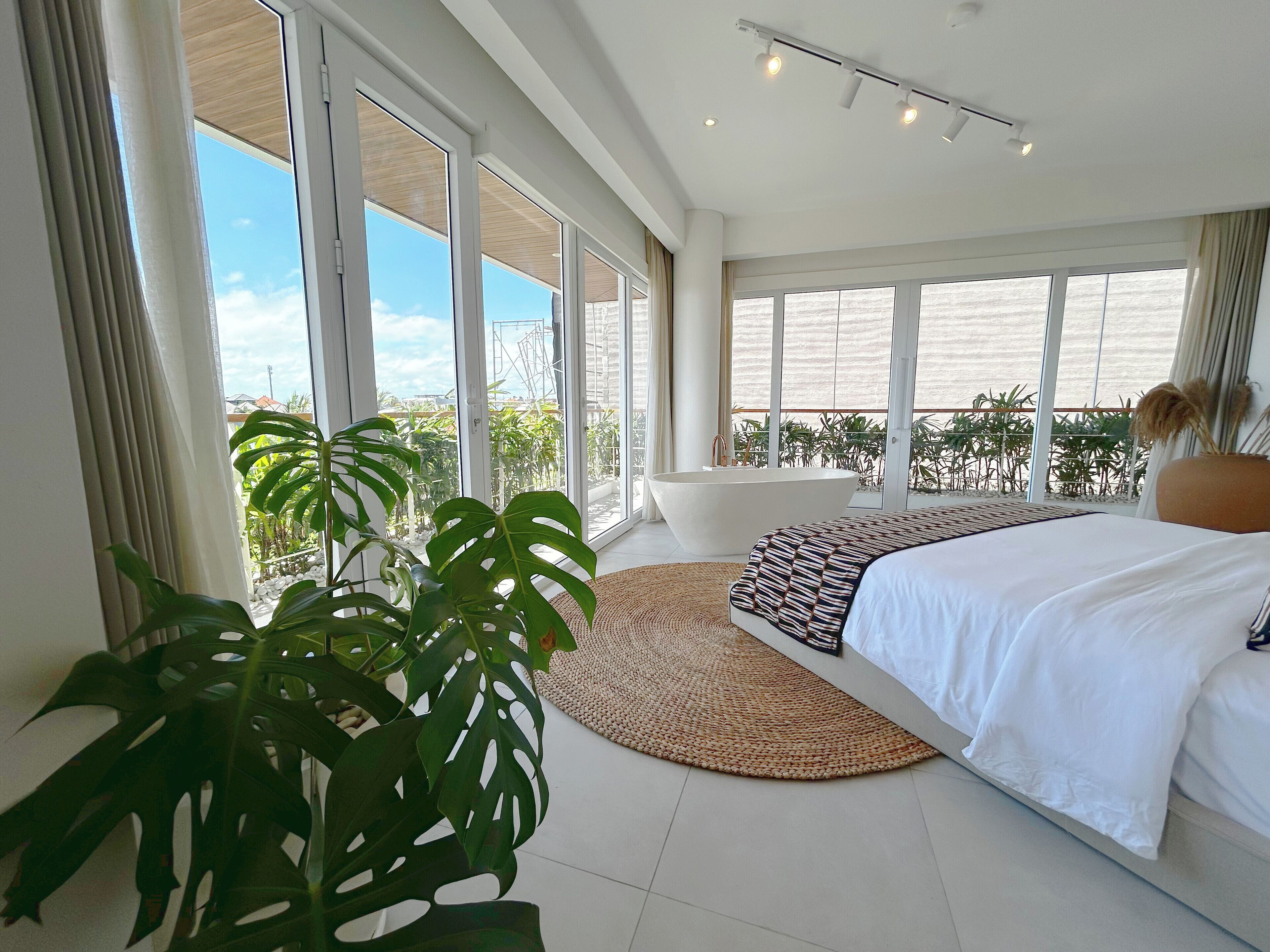 A modern bedroom with a large bed, a bathtub, and a view of the outdoors.