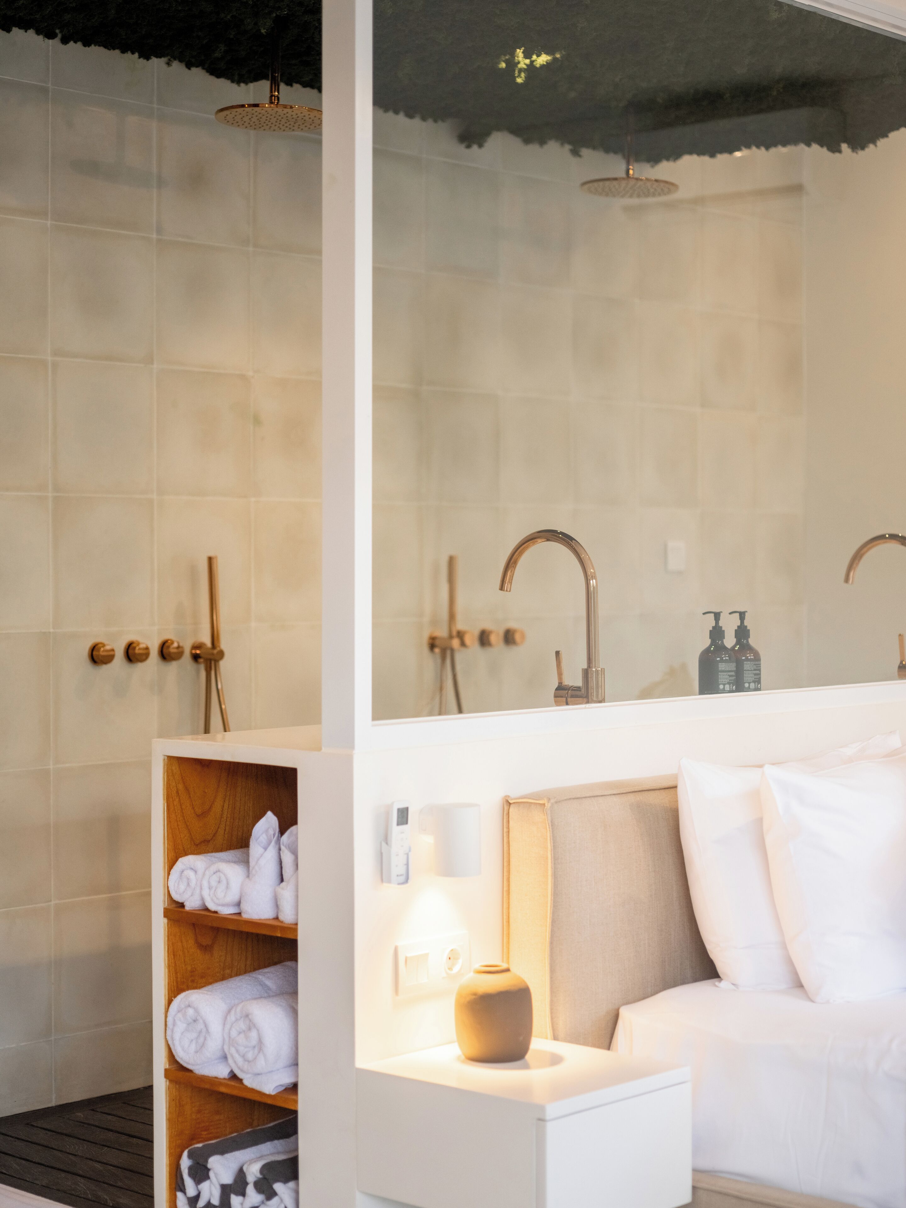 A modern bathroom with a shower, a toilet, and a sink. There is a wooden shelf with towels and a small table with a vase.
